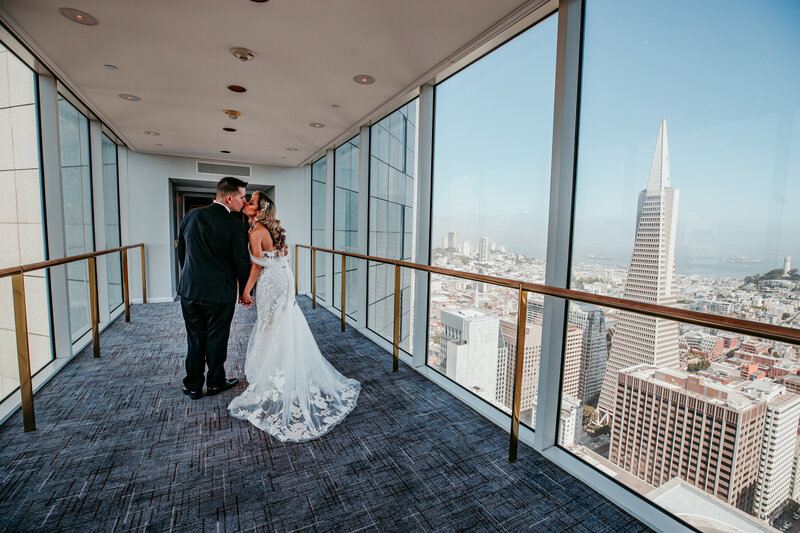 Bride and groom embracing inside the Four Seasons San Francisco at Embarcadero, with sweeping views of the city skyline and the Transamerica Pyramid, captured by San Francisco elopement photographer Kristin Smith.