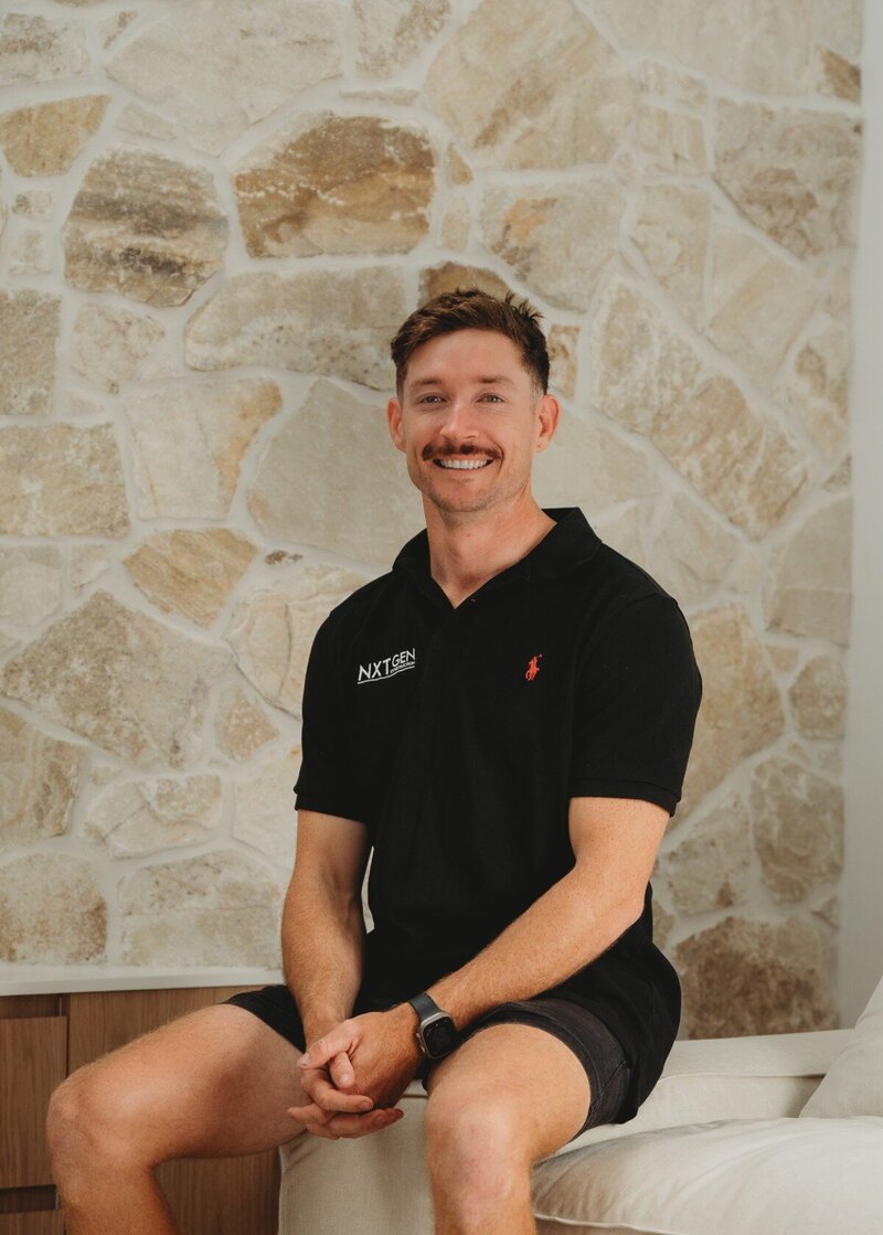 Trent Allen, founder of NXTgen Construction, sitting in front of a feature stone wall, representing the passion and craftsmanship behind every high-end residential project.