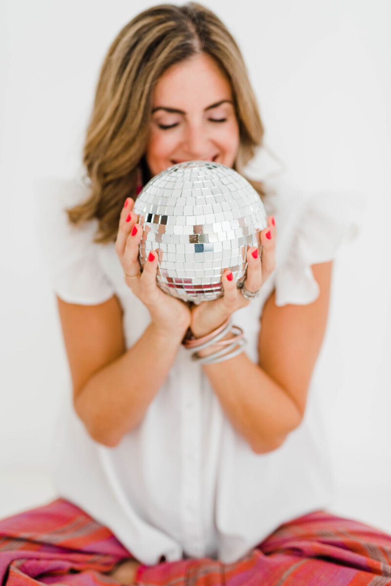 woman holding a small disco ball up to her face with red fingernails