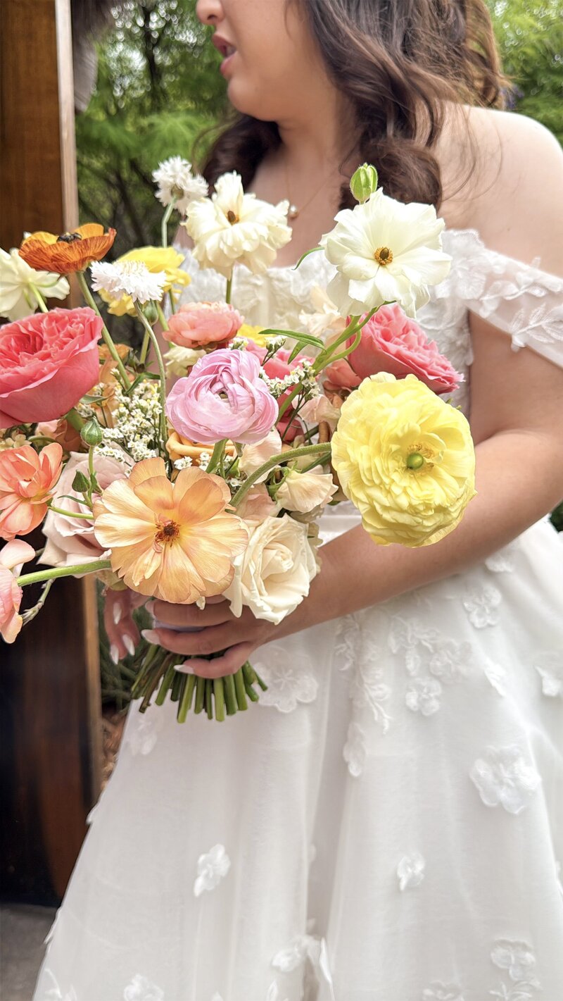 Bride holding her floral bouquet featuring yellow, pink, coral, and orange blooms at San Diego Safari Park San Diego Zoo Safari Park.