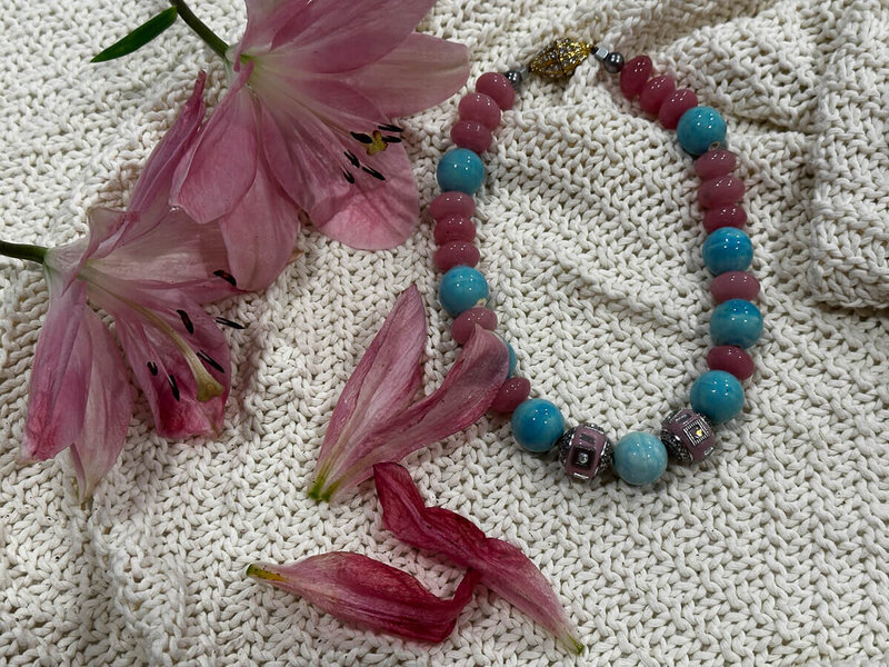Dawn Sky necklace by Nita Tin, an 8-inch pink and turquoise bead necklace with gold magnet clasp, displayed on a cream woven blanket with pink lilies.