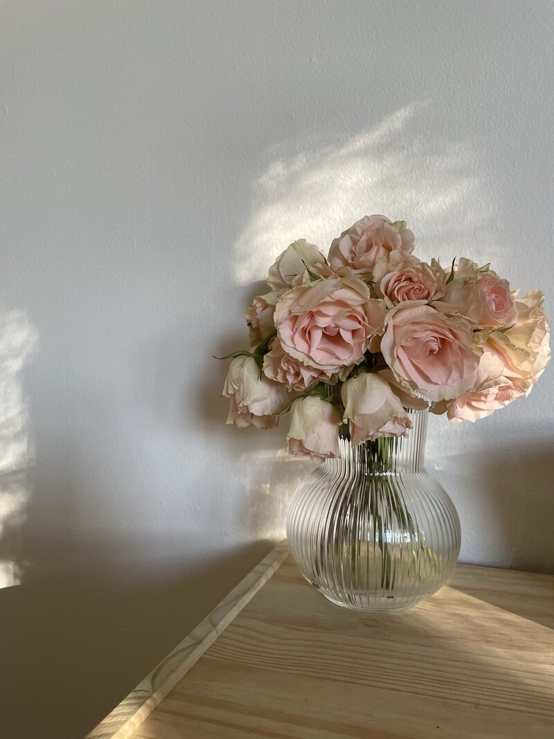 A person with long blonde hair sits on elegant brownstone steps, wearing a black outfit and white sneakers. They look down, creating a relaxed and contemplative atmosphere.