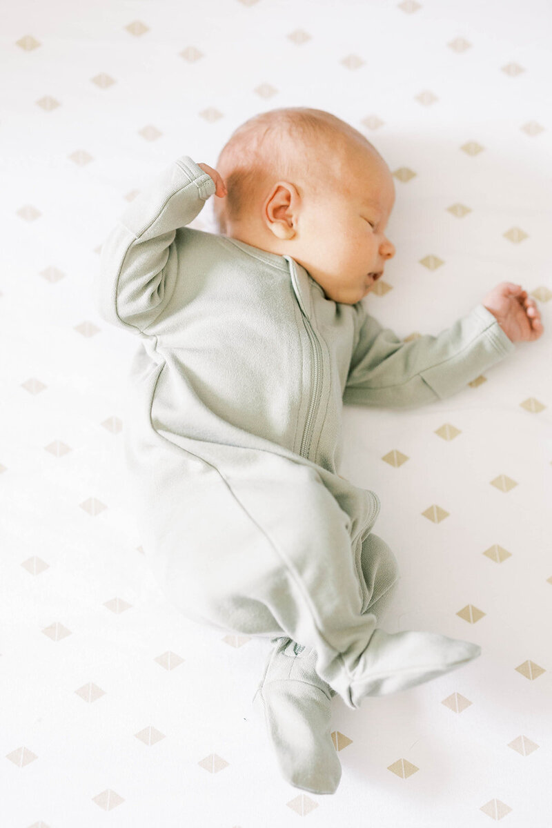Baby in green onesie lays down in crib in Pennsylvania nursery