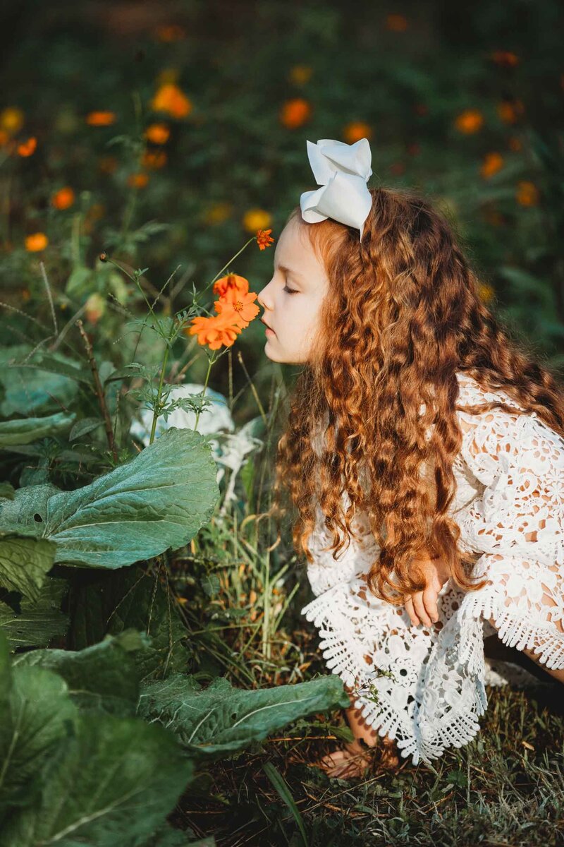 A sweet girl with red hair stops to smell the flowers during her family portraits at Turnipseed Nursery in Fayetteville, Georgia.