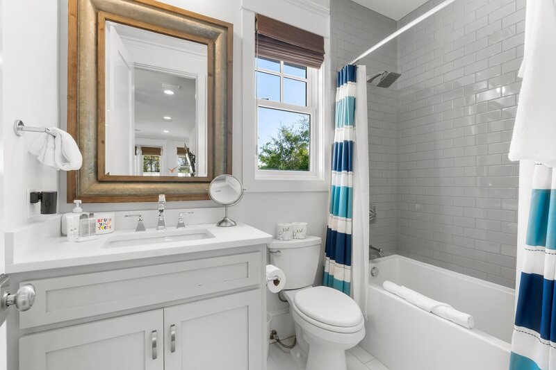 Cheerful guest bathroom with a shower/tub combo, striped coastal shower curtain, and wood-framed mirror at Panama City Beach vacation home.