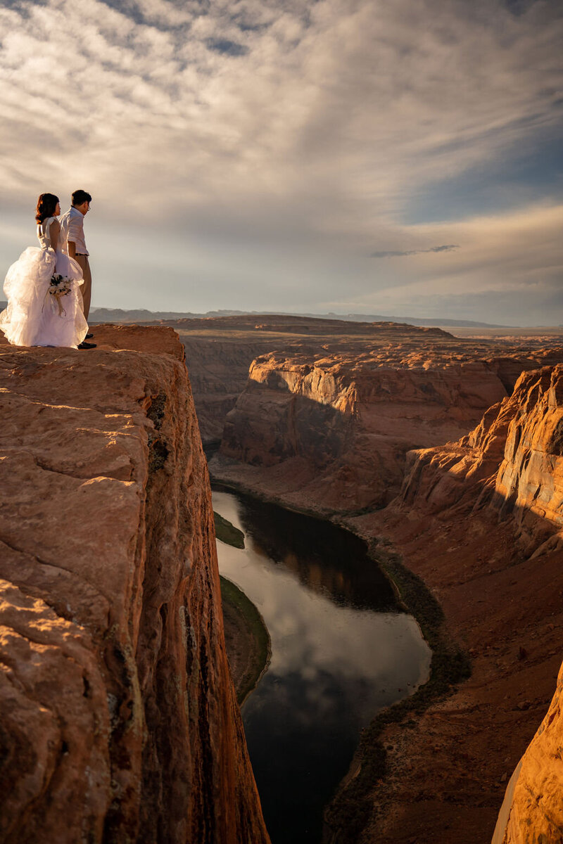 Couple stands on the edge in wedding attire - Horseshoe Bend Wedding