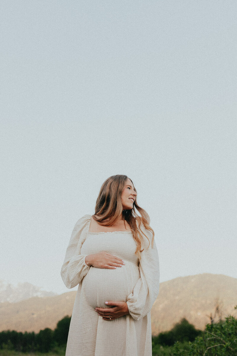 photo of a pregnant women cradling her baby bump and smiling off camera taken by a langley newborn photograher