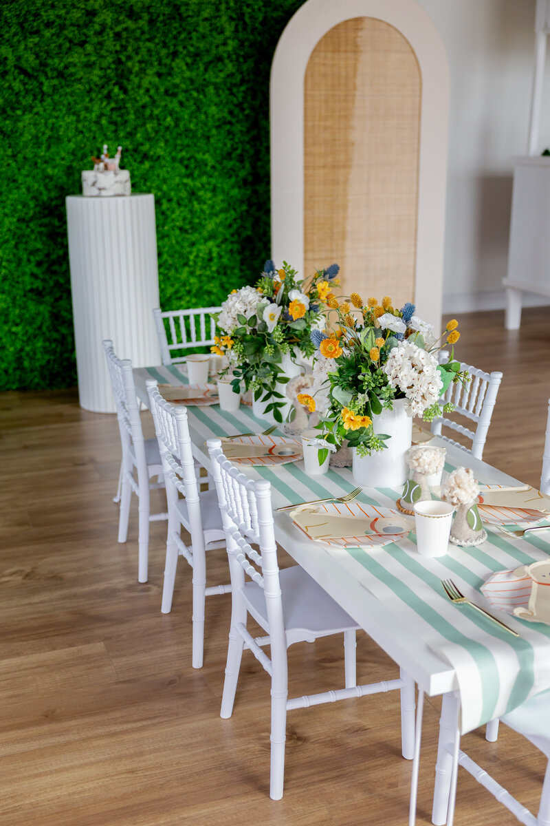 Kids white table and chairs, table runner, flower arrangements and dog paper plates.