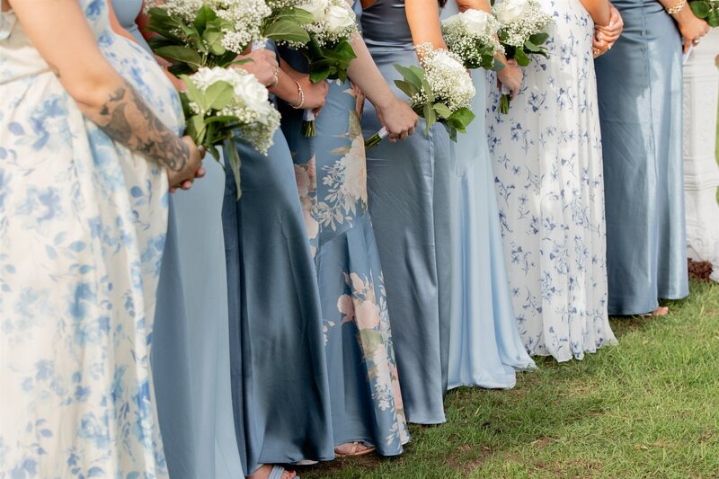 Bridesmaids in blue floral dresses holding bouquets before the ceremony at a Raleigh wedding, photographed and filmed by Moments by Hiba.