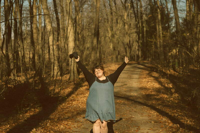 A photographer holds her camera in a snowy forest, smiling at her equipment