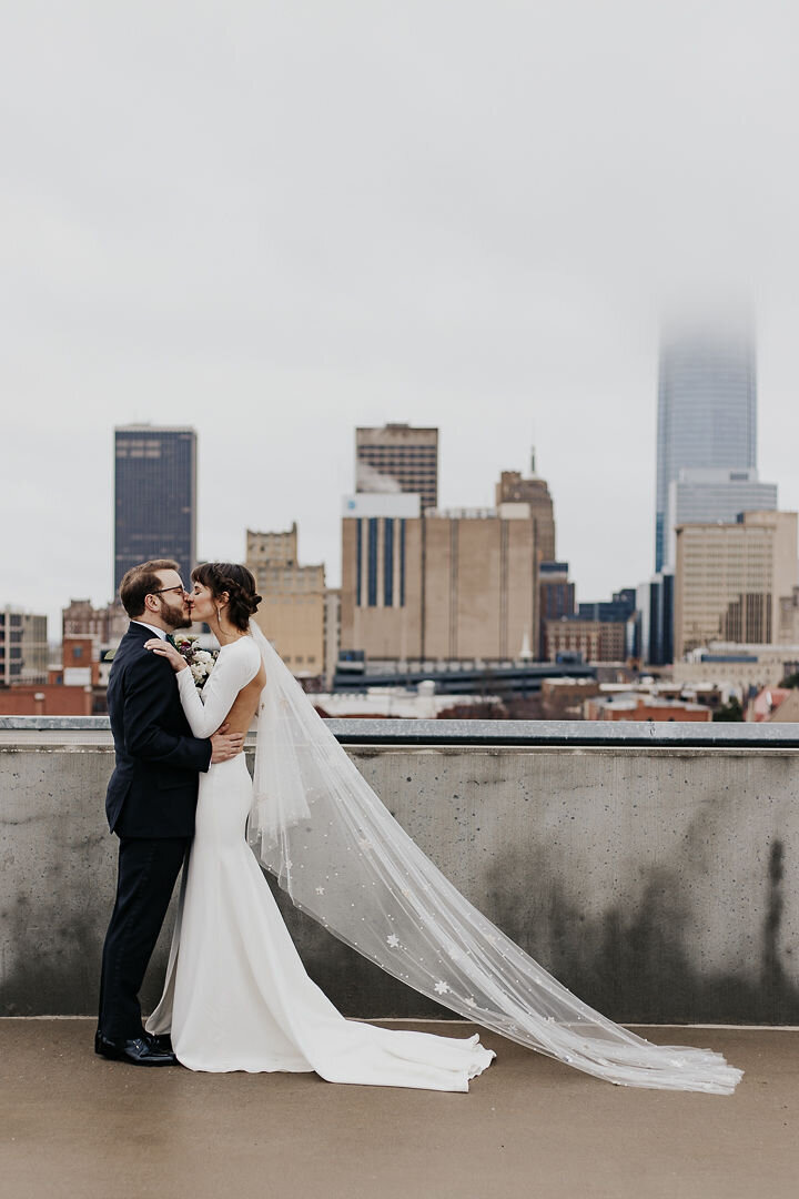 Bride and Groom standing on a rooftop kissing with the city in the background