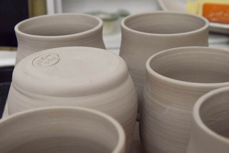 Bisque-fired ceramic mugs sit on the studio table waiting to be glazed