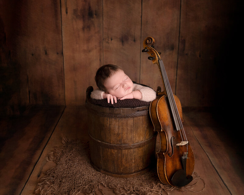 Nyfødt baby sover fredelig ved siden av en fiolin – et kunstnerisk nyfødtportrett av Fotograf Gina Englund, Oppegård. Formidler ro, varme og nostalgi.