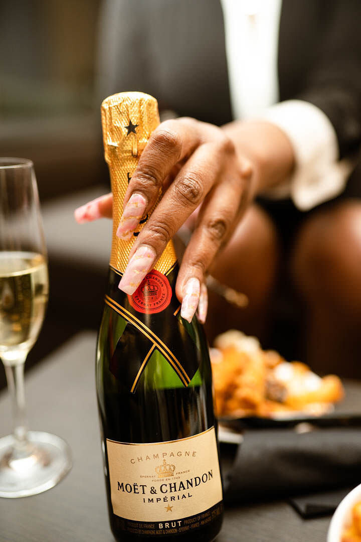 A black woman holds a bottle of champagne in front of the camera