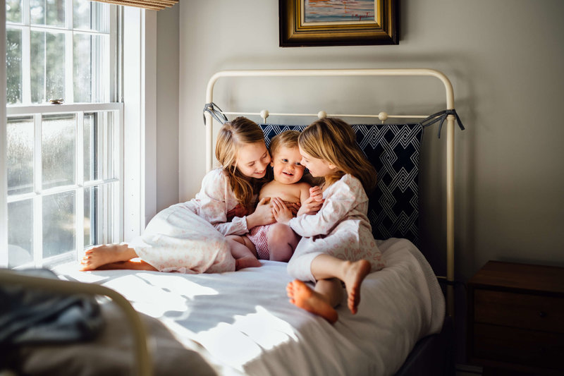 two sisters on bed with baby brother