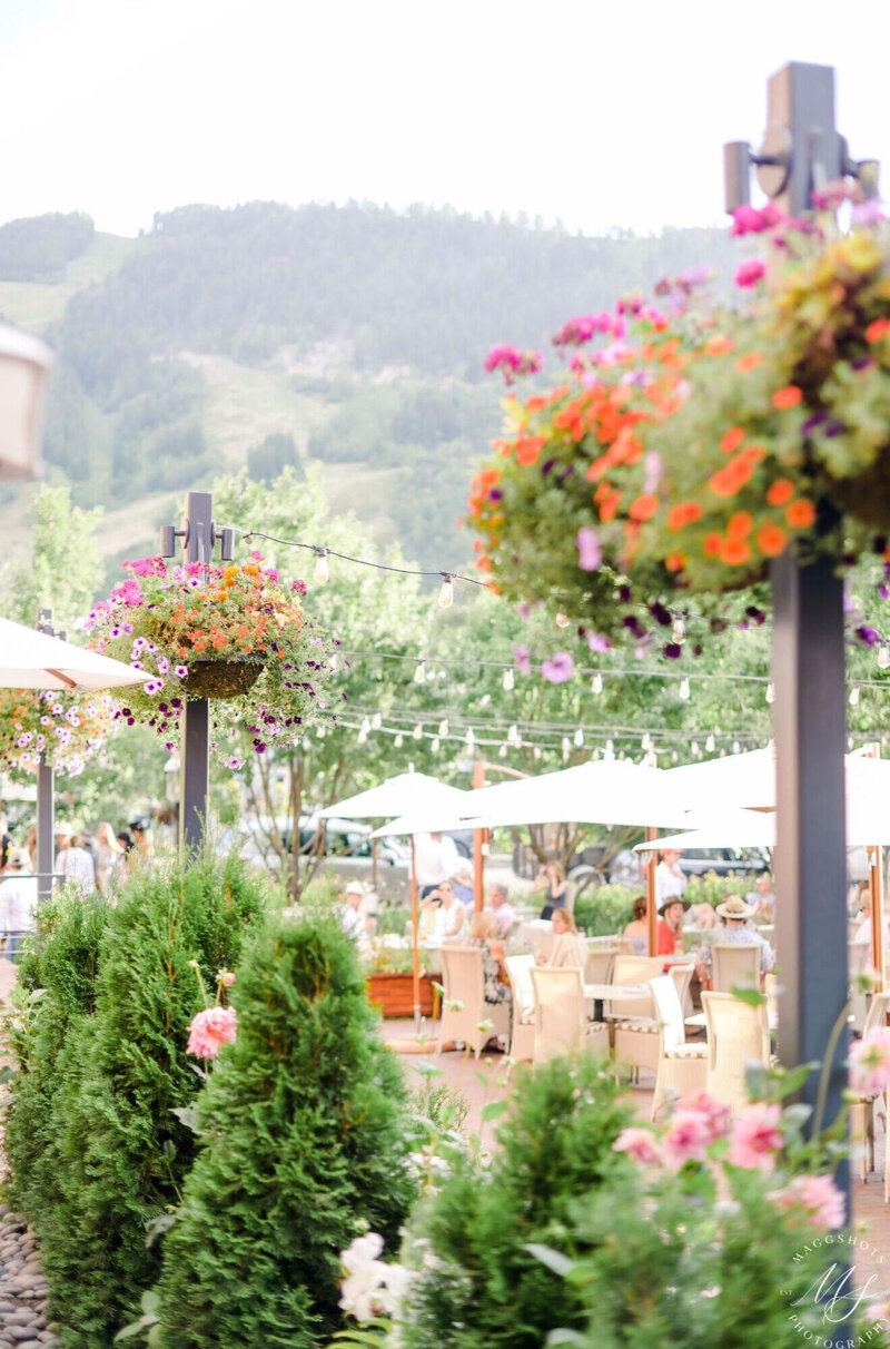 An outdoor event venue in Aspen with string lights, umbrellas, tables and chairs with a view of mountains and colorful flowers