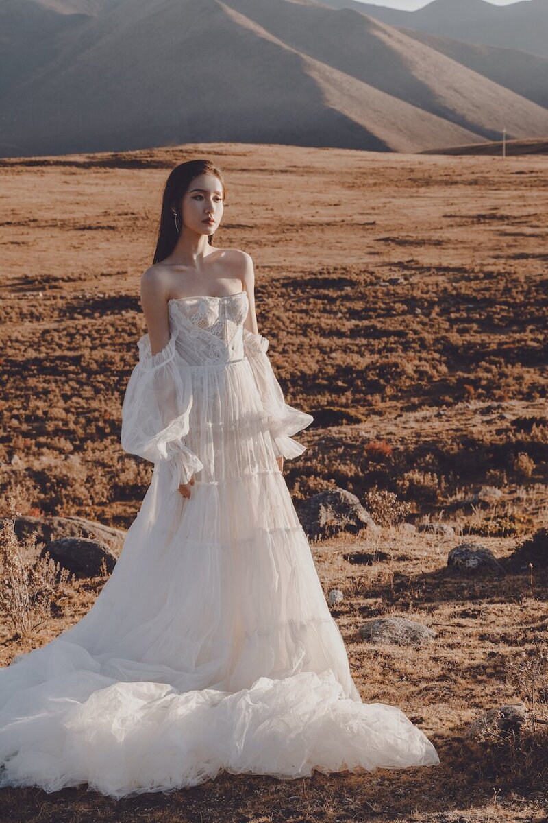 A bride photographed in the golden evening light in a wild field with. mountains in the background.