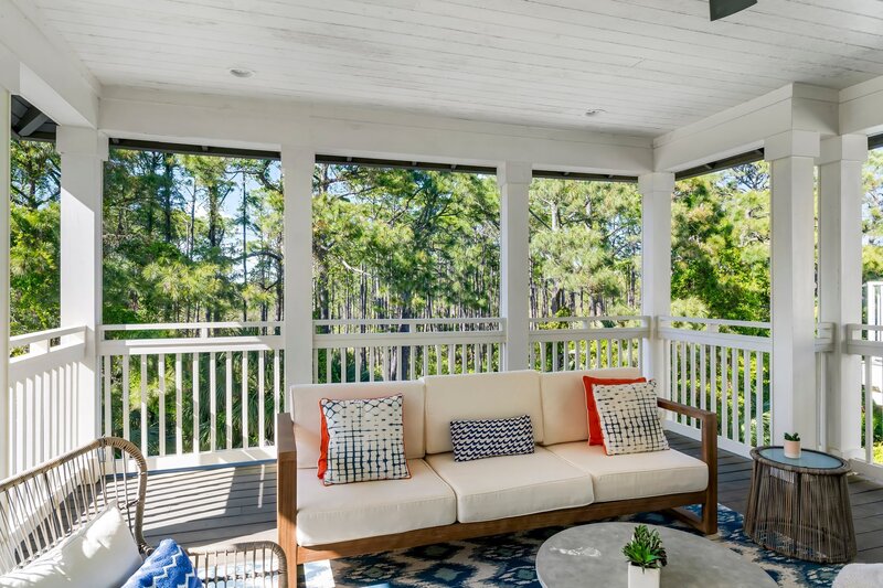 Comfortable outdoor seating with modern decor and serene tree views from screened balcony