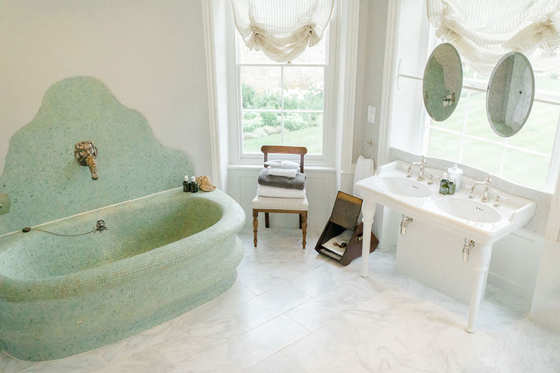 Mosaic bath with silver tap, marble floor, double sink and view over gardens