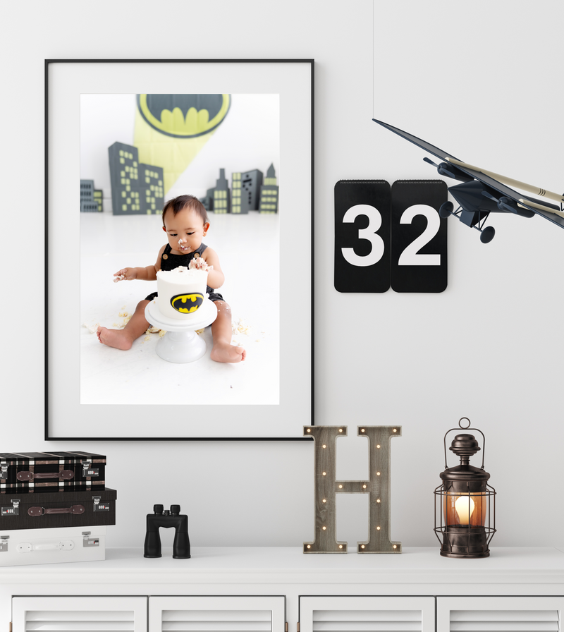 A batman themed fine art toddler cake smash photo hangs on a bedroom wall