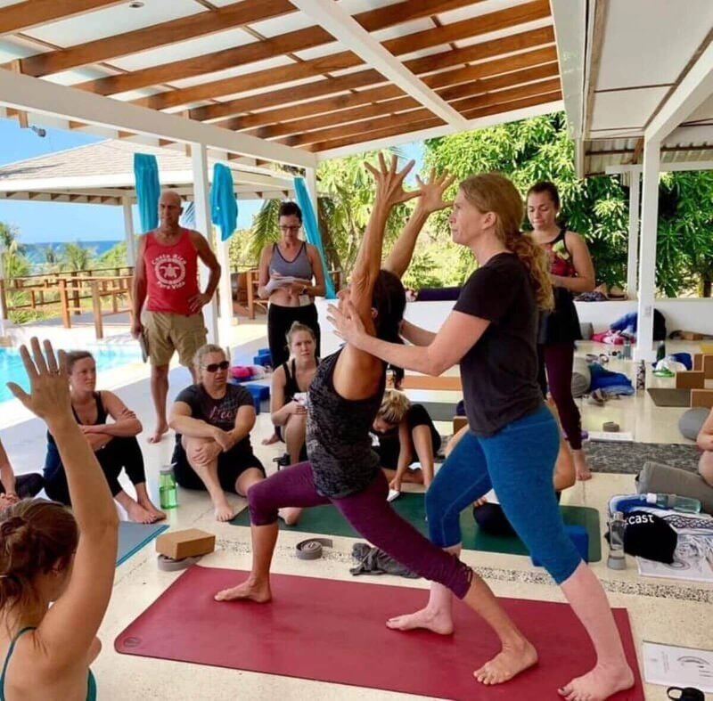 Teachers demonstrate hands-on assists to a class on the yoga deck during yoga instructor certification in Costa Rica