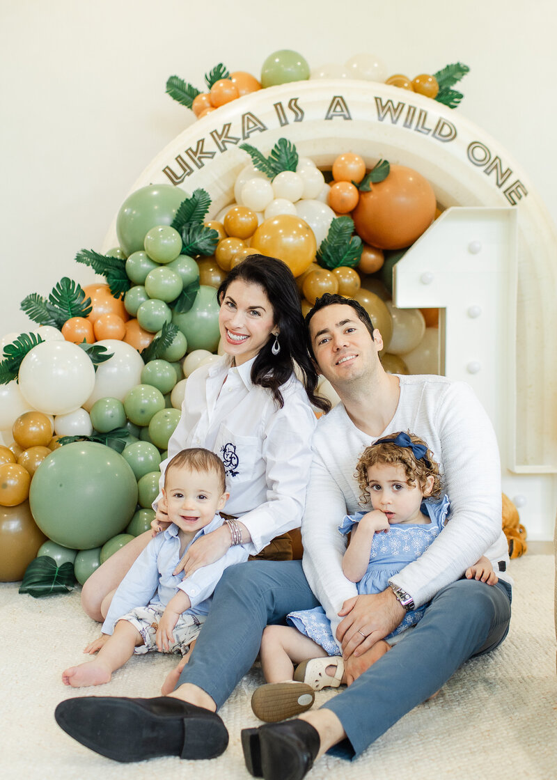 first birthday milestone photo featuring whole family and balloon garland.