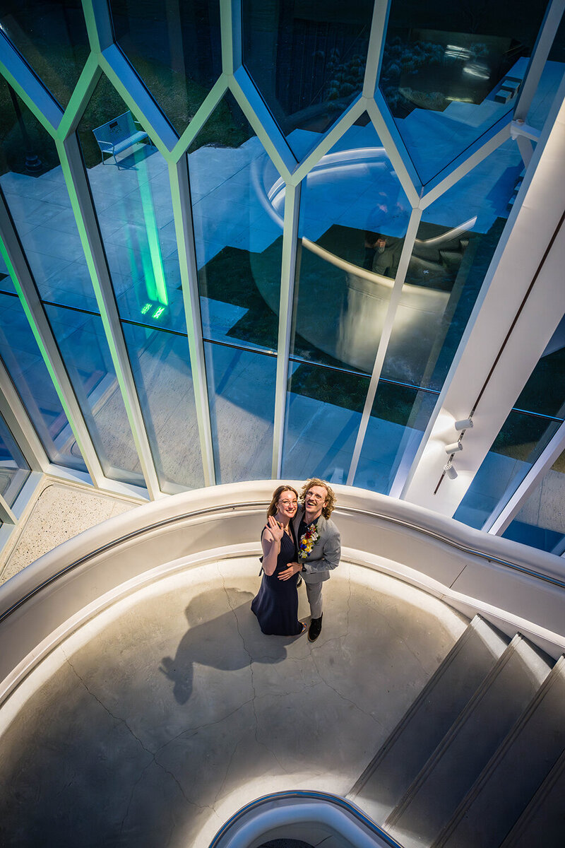 A couple embraces on the Moss Arts Center stairwell for their first dance. The pair pause to look up, smile, and wave at their photographer (not photographed) for a photo.