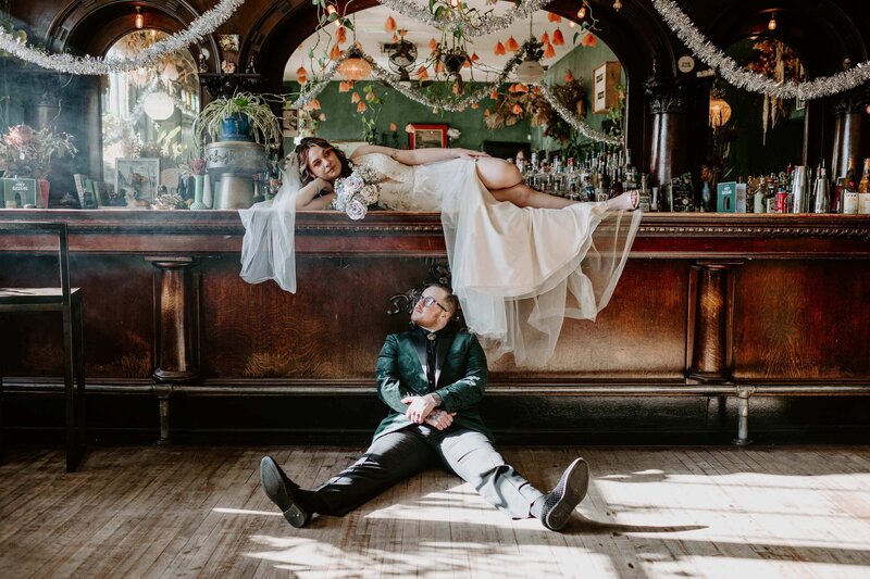 Bride Lounging on Bar With Partner Sitting Below