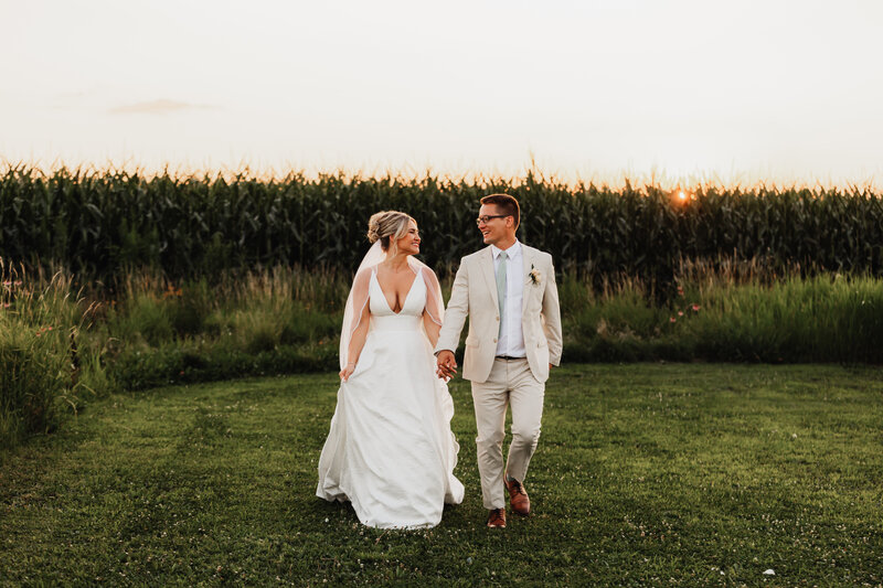 A wedding couple hold hands and frolic in an open field.