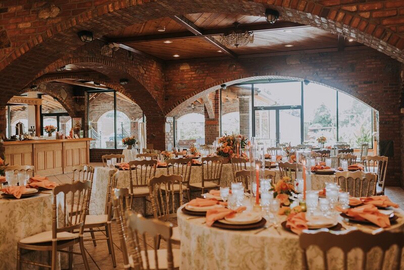 A decorated reception space with round tables, floral centerpieces, candles, and gold chairs is set in the Century Room at Grbic Events in St. Louis.