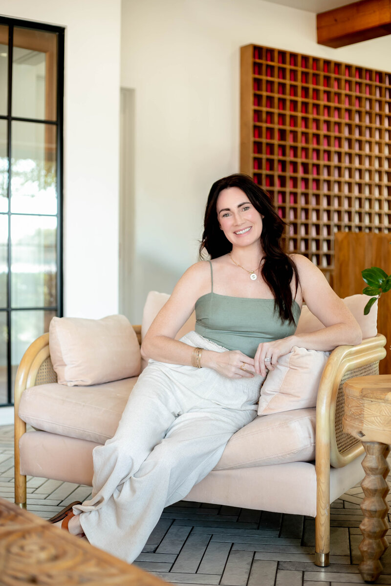 woman seated in oversized pink chair smiling looking welcoming to chat about holistic health for women in perimenopause