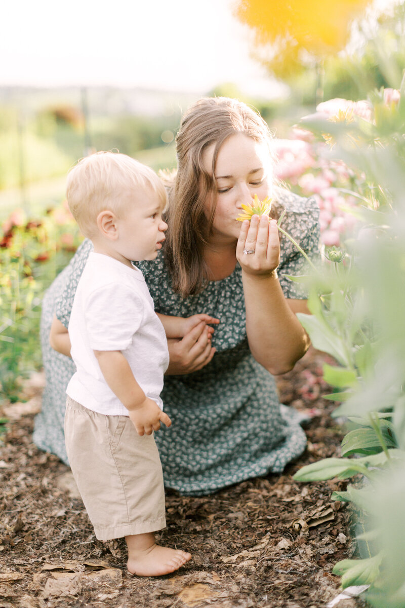 Mother smelling flowers with her toddler son in a flower garden