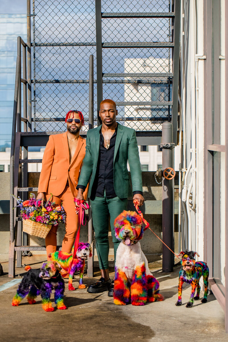 Luxury black couple engagement  session wearing pink outfits from fashion nova standing in front of a vintage Aston Martin with pink florals cascading out of the door by pop out decor and make up by pretty faces studios and a hair by Chelle of chelledidit and candy forever hair