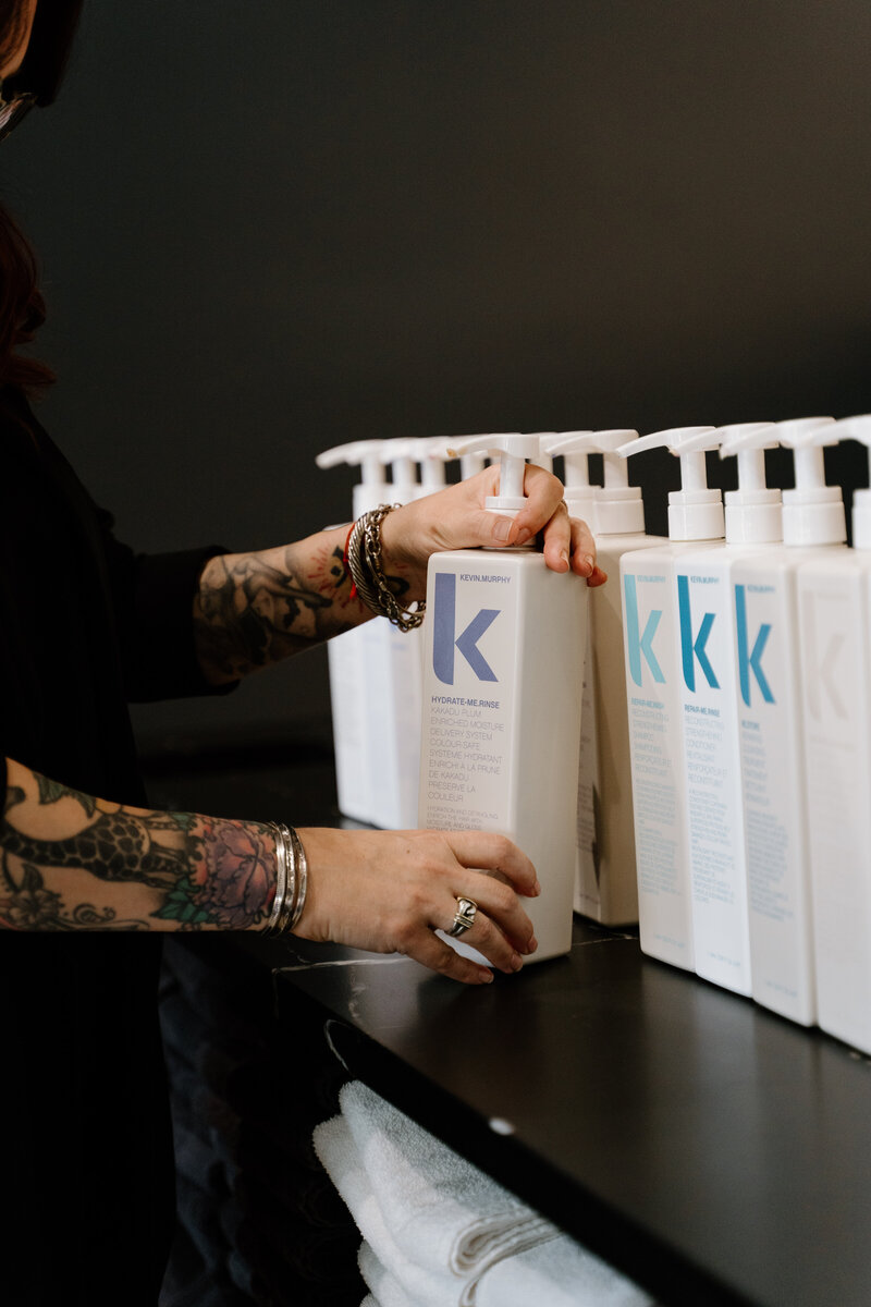 Brand photo of tattooed arms holding Kevin Murphy shampoo in hair salon.