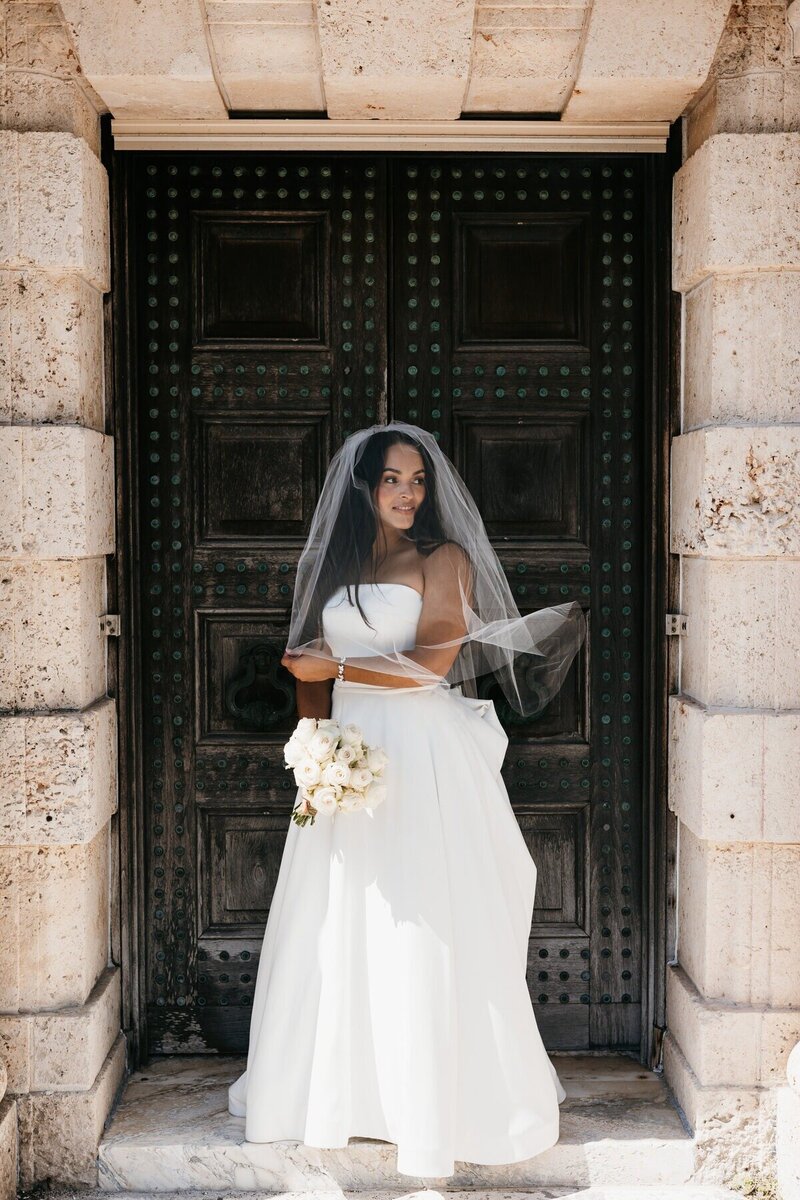 Bride standing in a doorway holding a bouquet in Naples, Florida, image captured by a Naples wedding photographer, Priscila Del Cristo. 