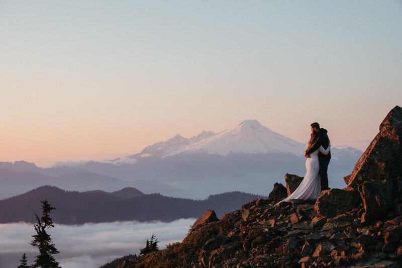 Elopement Photo Ideas | Bride and Groom watch the sunset from a mountaintop with a huge mountain behind them