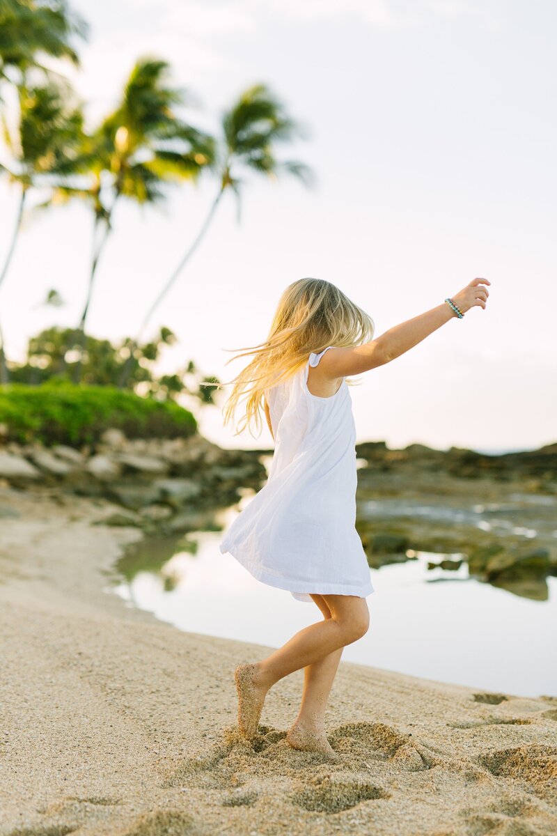 girl in a white dress twirls in the sand at Paradise Cove Oahu