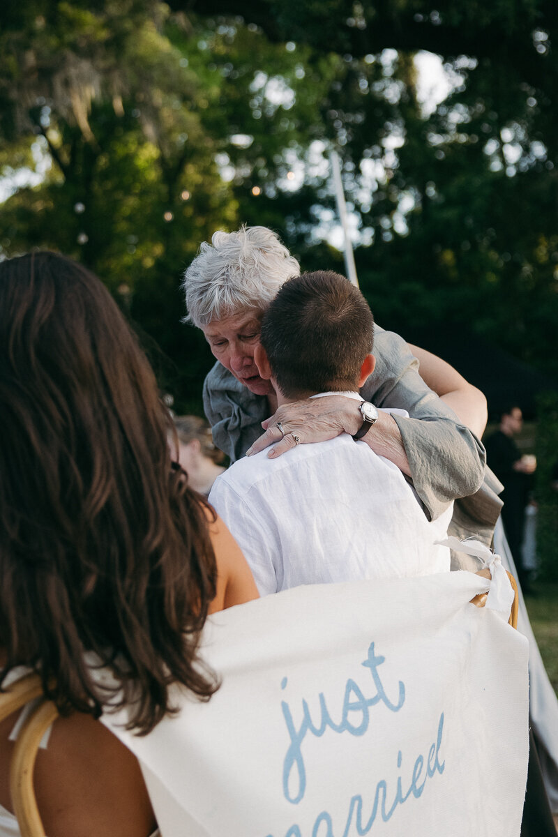 bride and groom embracing grandmother as she cries