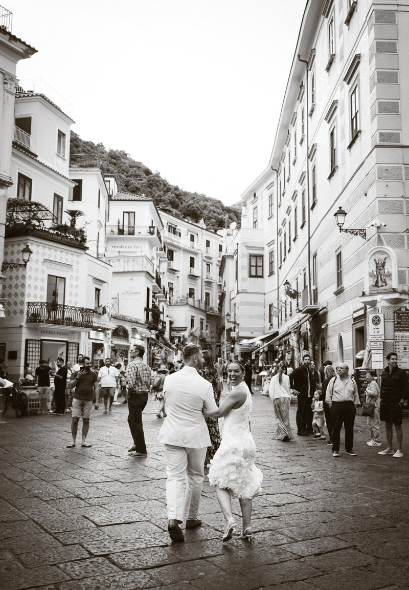 Couple posing near vibrant buildings with the Amalfi Coast coastline behind them.
