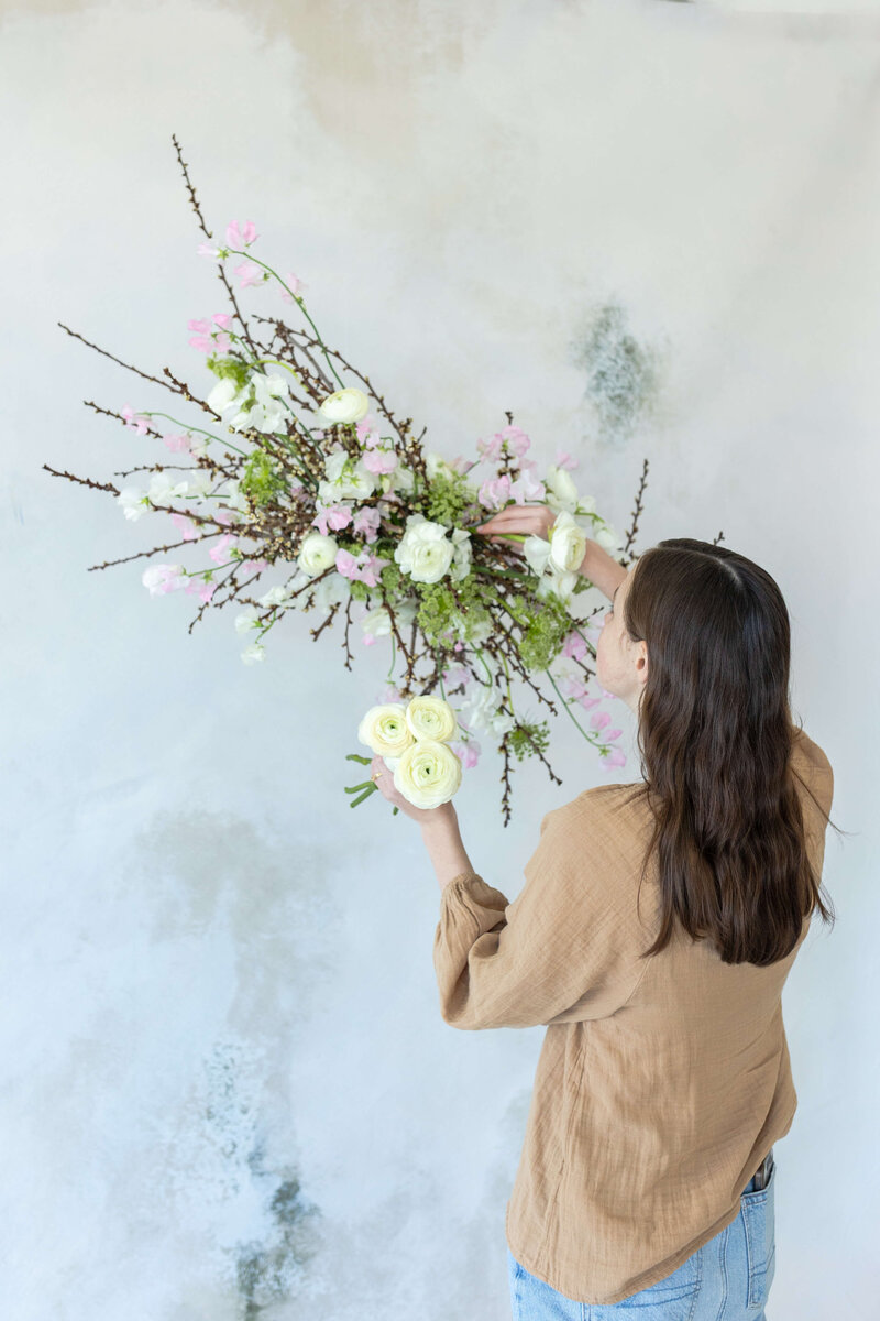 woman putting flowers in overhead installation