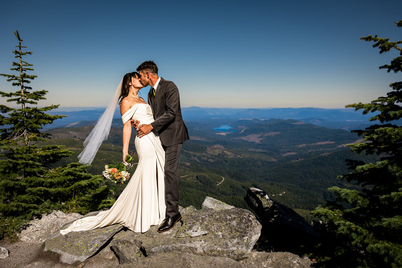 Bride and groom standing on a cliff in Yosemite park at sunset.