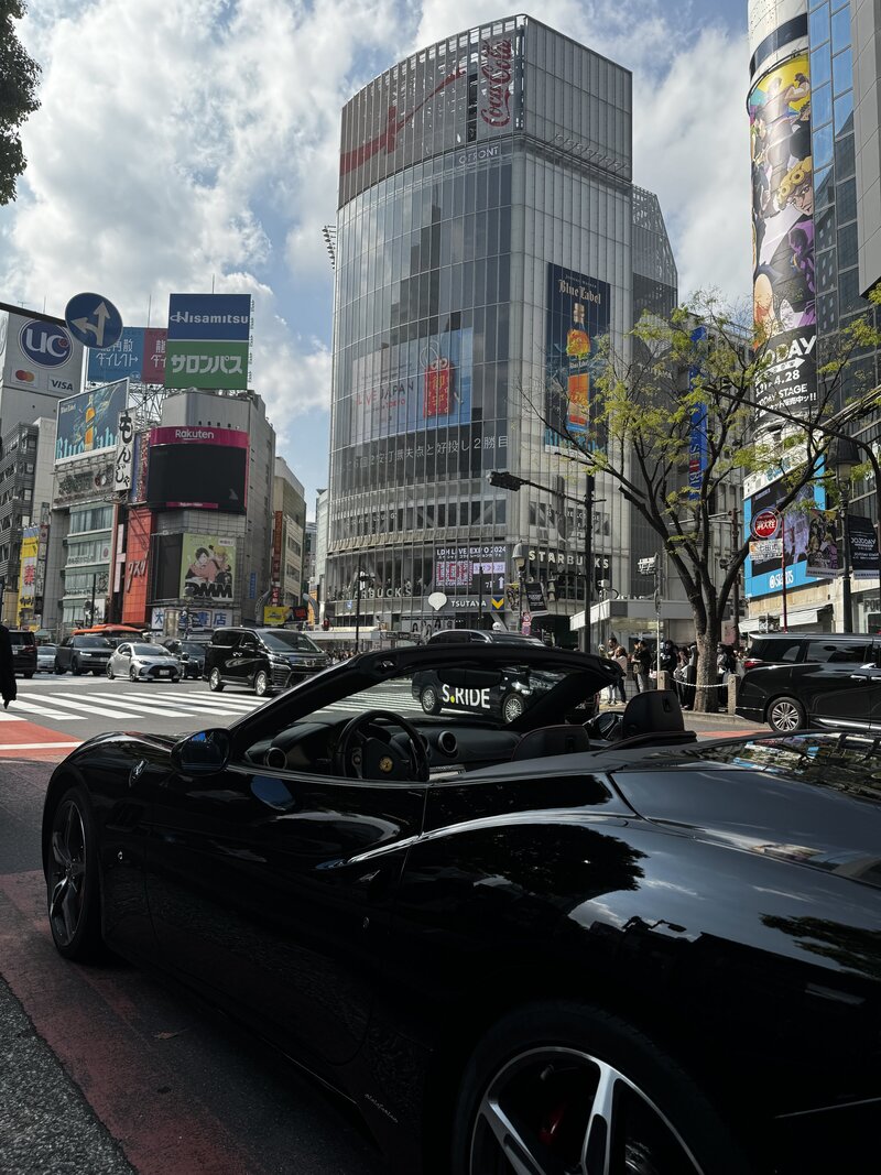 A sleek black Ferrari California from Tokyo Luxe Drive cruises through the iconic Shibuya Crossing, blending high-performance luxury with the electric energy of Tokyo's city streets.

