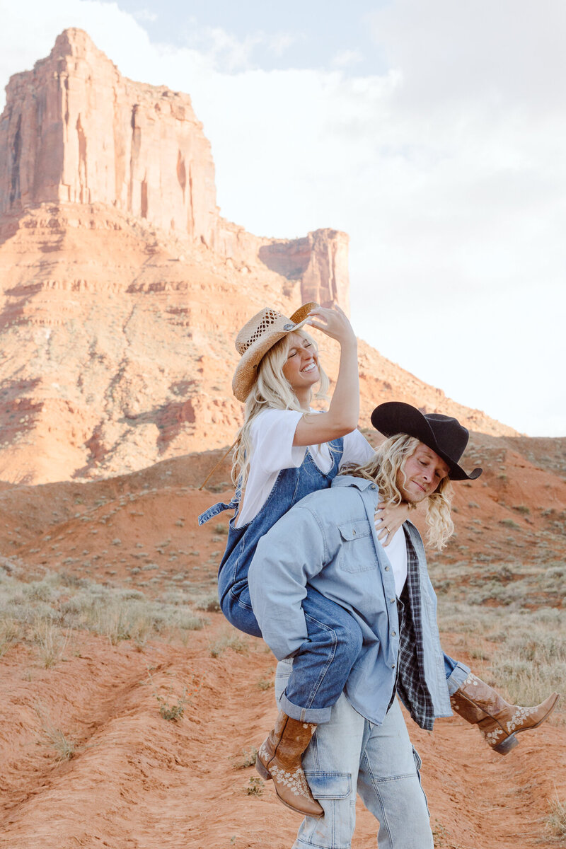 A couple smiling will taking a piggyback stride in Moab, Utah
