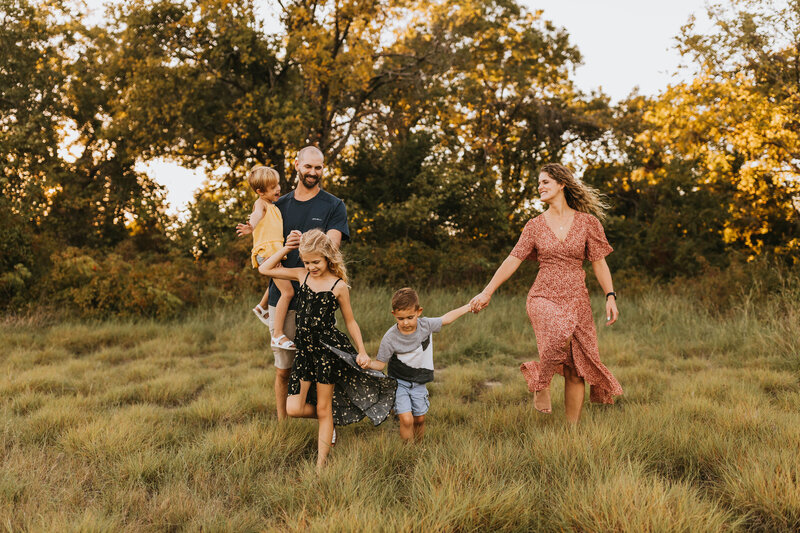 family in colorful outfits walking through a green field at sunset