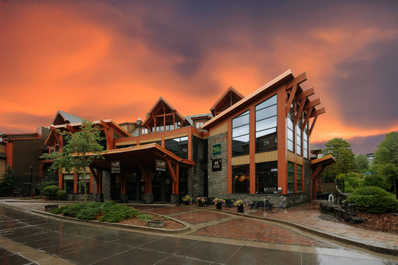 Contemporary timber-and-glass exterior of Solara Resort Accommodation in Canmore, Alberta, featuring striking architectural beams, stone accents, and large windows with views of the surrounding Canadian Rockies.