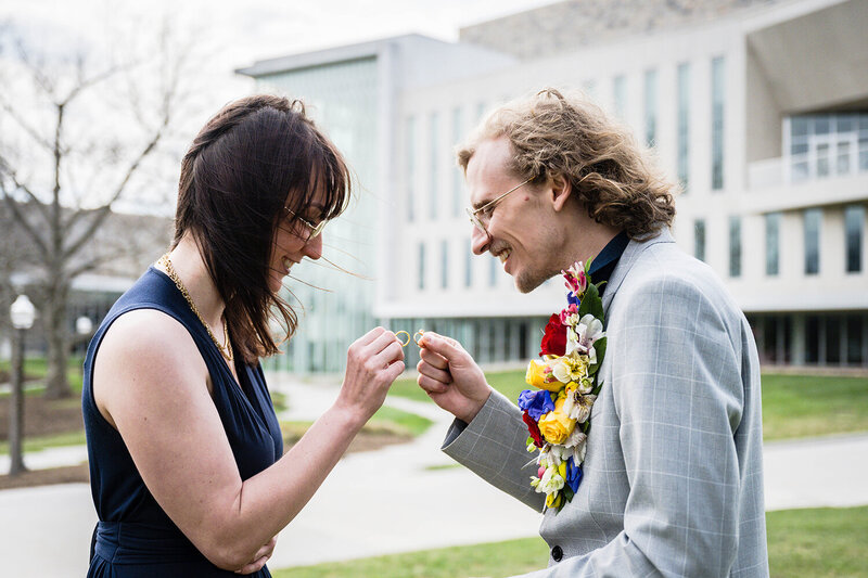 A bride and groom on their elopement day "clink" their rings together during a ceremony in front of the Moss Arts Center at Virginia Tech in Blacksburg, Virginia.