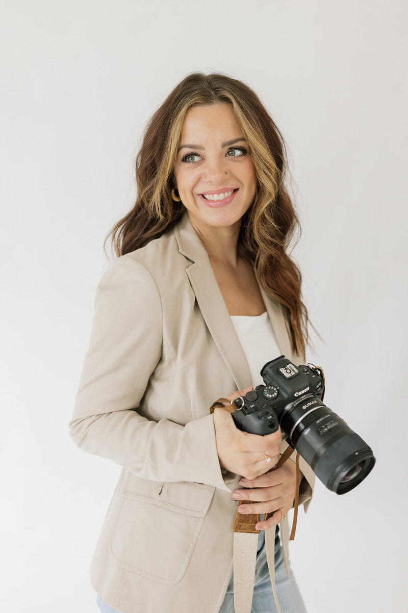 Headshot of photographer  Charity White , posing in a seated position, smiling, and holding a camera