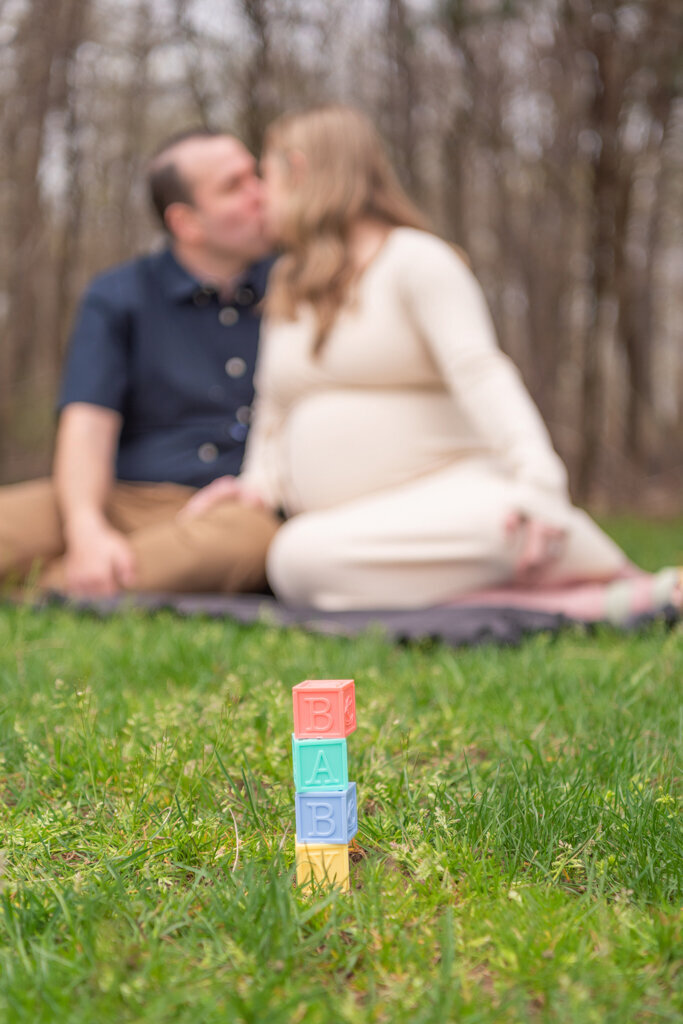 A couple kissing in the background and foreground has a block spelled out the word "baby".