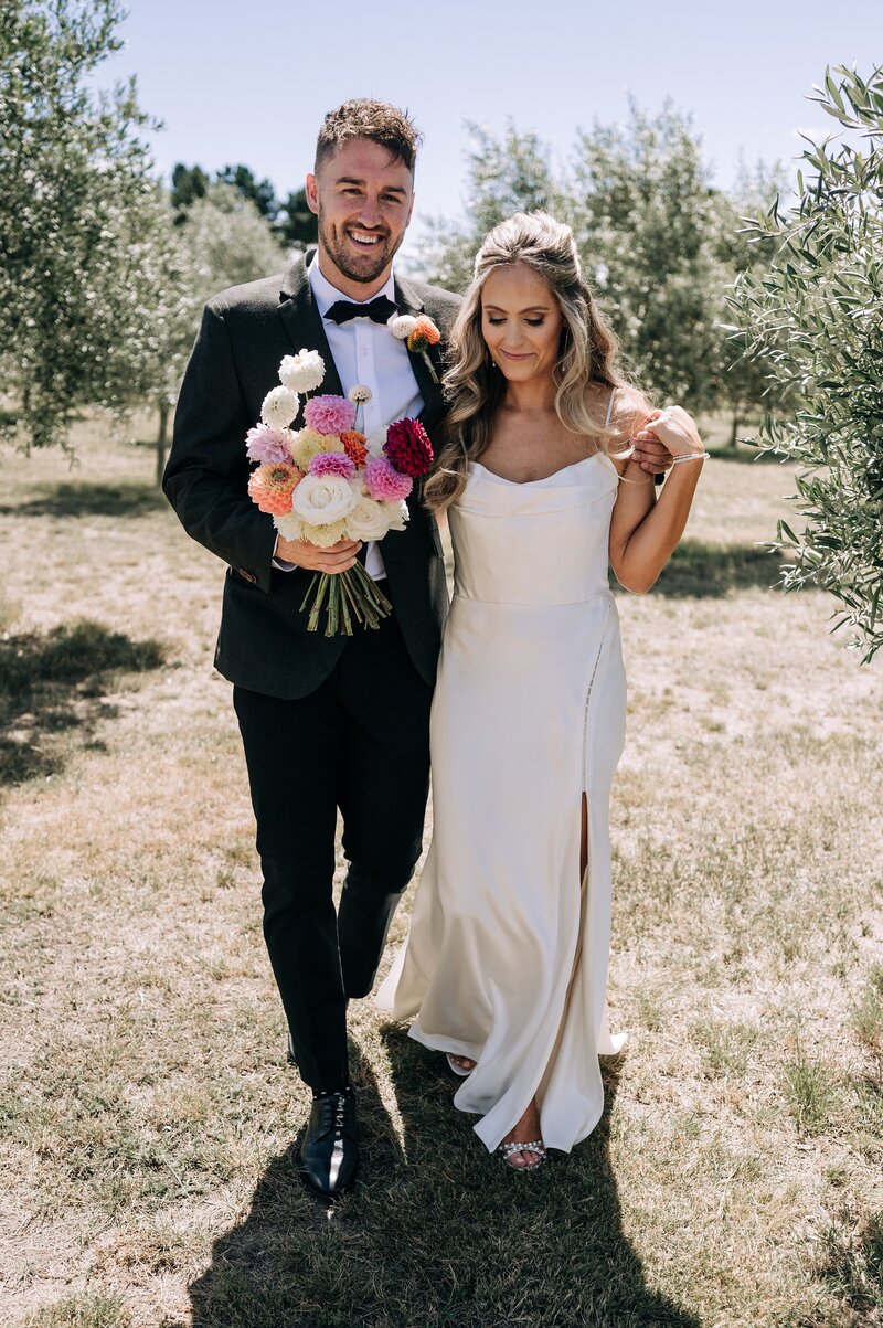 a bride and groom walk through an olive grove in waipara north canterbury on their wedding day