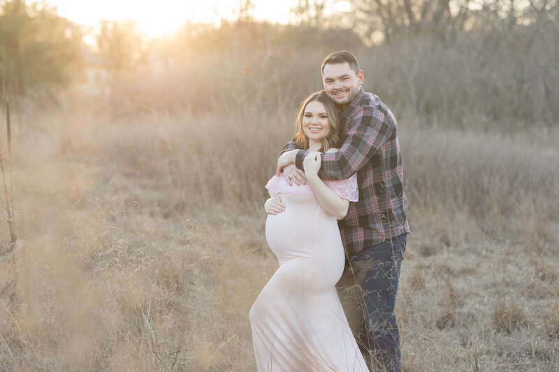 A happy couple poses for their maternity session with a stunning sunset